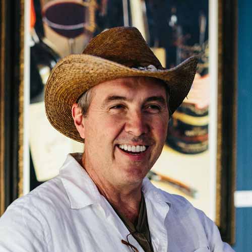 Painter Thomas Arvid smiles as he presents live painting in front of a completed wine painting in the background.