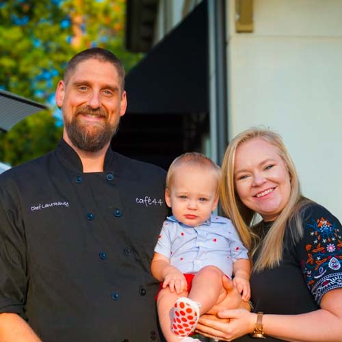 Photo of Lane Raney, Chef and Owner of Cafe 44, smiling with his wife and baby son.