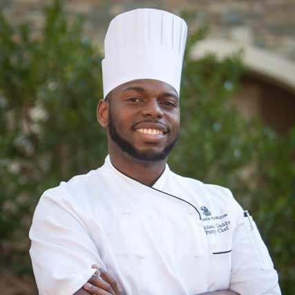 Portrait of The Ritz-Carlton Reynolds, Lake Oconee Pastry Chef, Micheal Gaddy, wearing a chefs hat and smiling at the camera.
