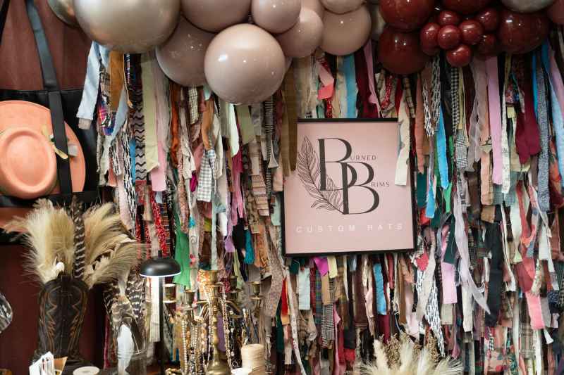 Strips of fabric hang amongst hats, feathers and other hat accessories at the booth for burned brims hat customizing table at the market place.